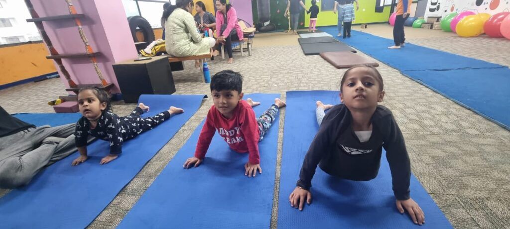 Kids practicing yoga on blue mats in a spacious indoor play gym, promoting health and balance.